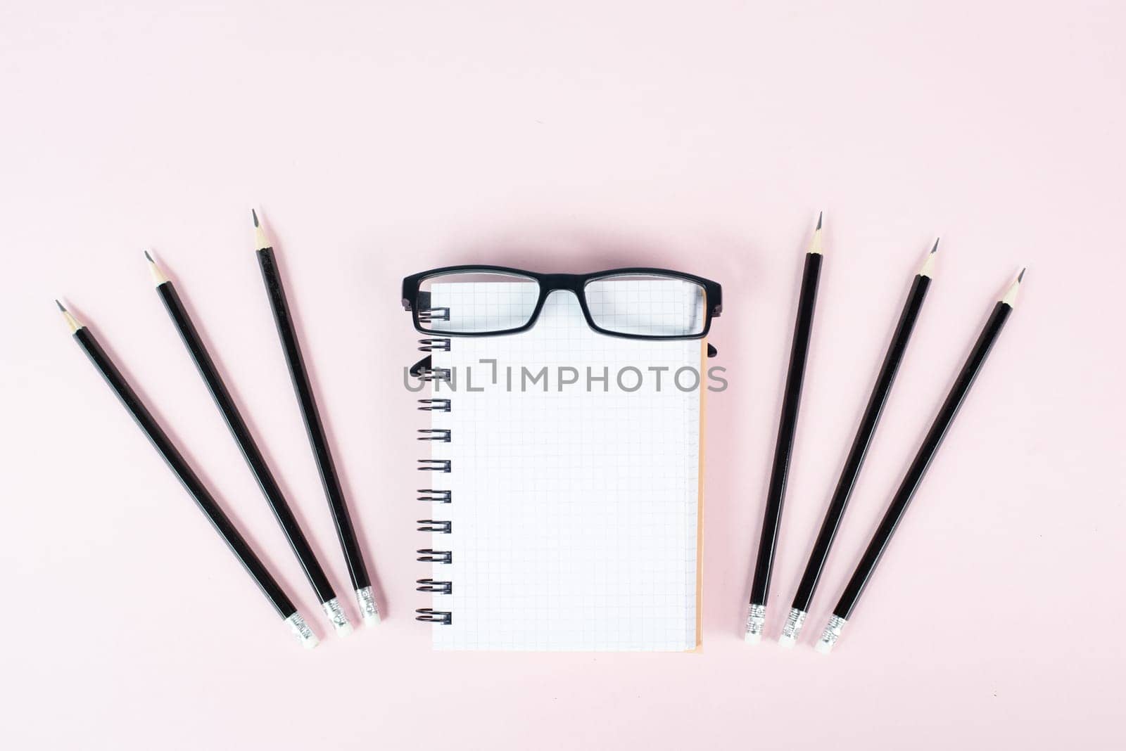 Empty notebook with pencils and eyeglasses on a rose background, brainstorming for new ideas, writing a message, home office desk
