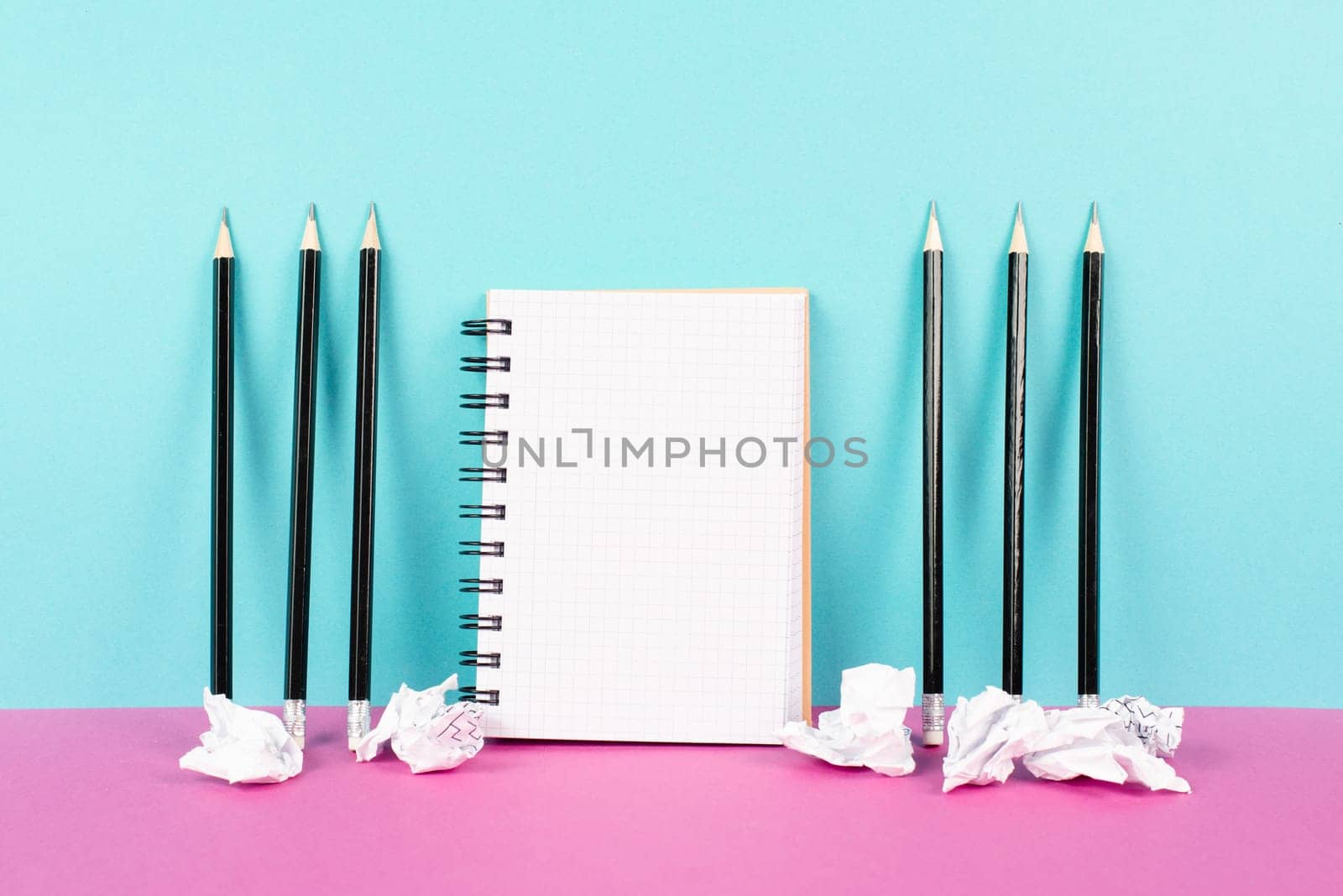 Notebook with copy space, pencils and crumpled up paper on a pink and blue background, brainstorming for new ideas, writing a message, home office desk