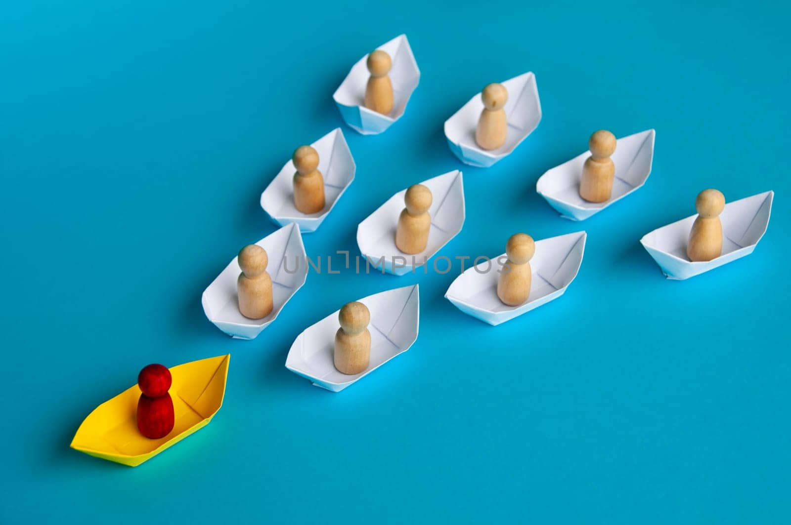Leadership Concept - Red people figure on yellow paper ship origami leading the rest of the people figure on white paper ship. Copy space.