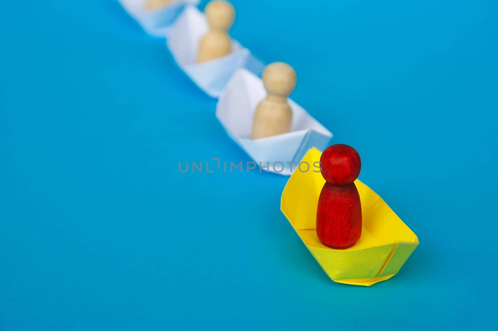 Leadership Concept - Red wooden figure on yellow paper ship origami leading the rest of the figure on white paper ship. Copy space.