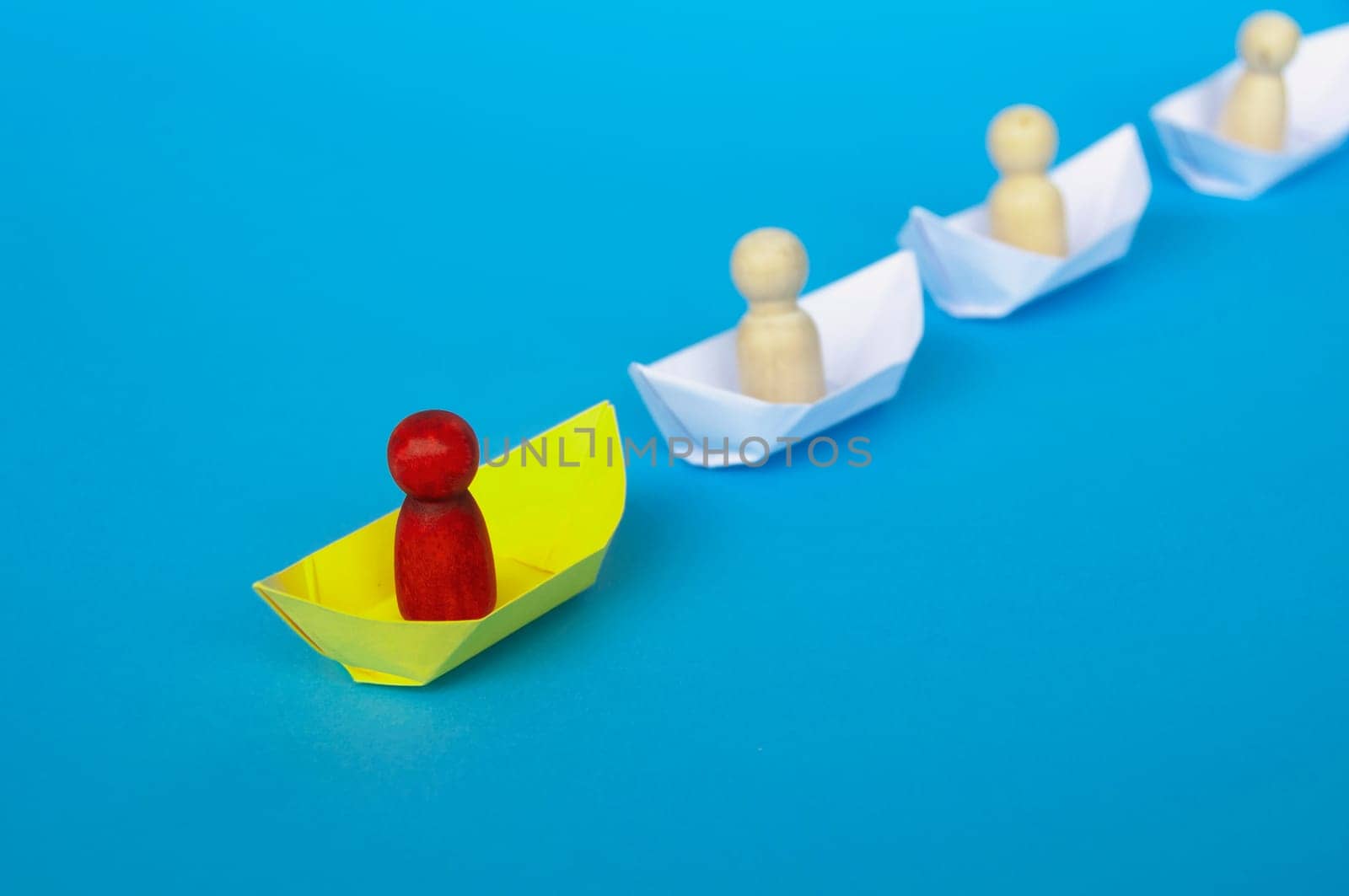 Leadership Concept - Red wooden figure on yellow paper ship origami leading the rest of the figure on white paper ship. Copy space.