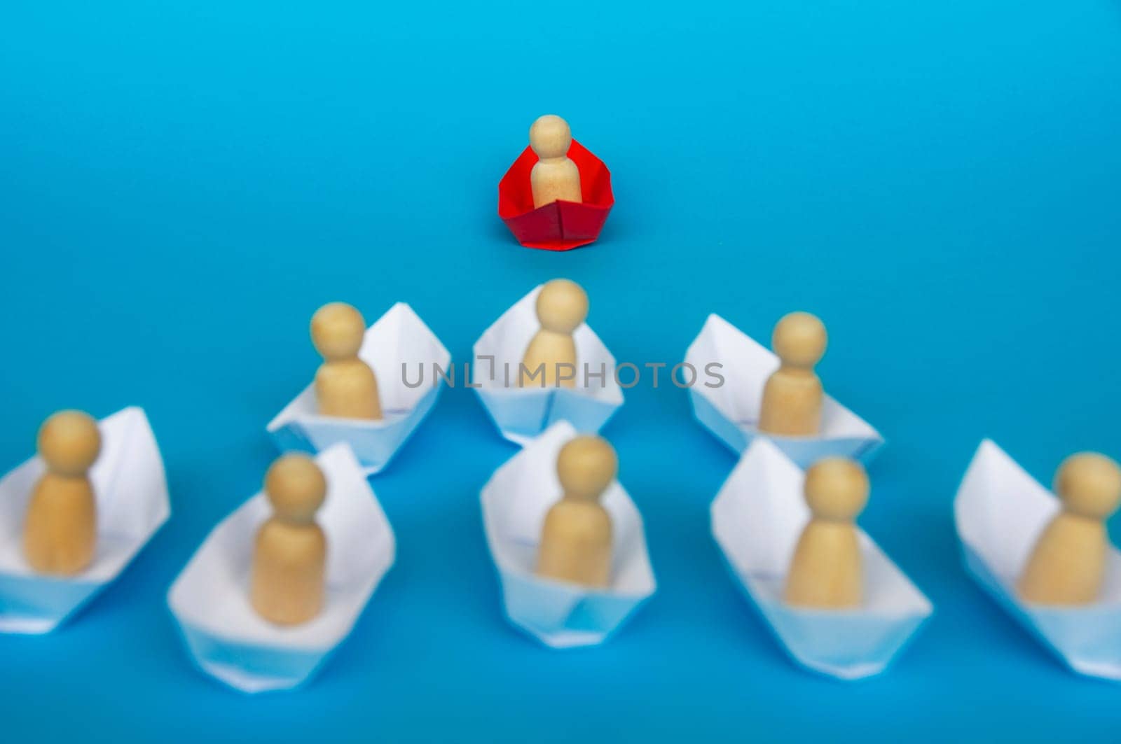Leadership Concept - Wooden figure on red paper ship origami leading the rest of the figure on white paper ship. Copy space.