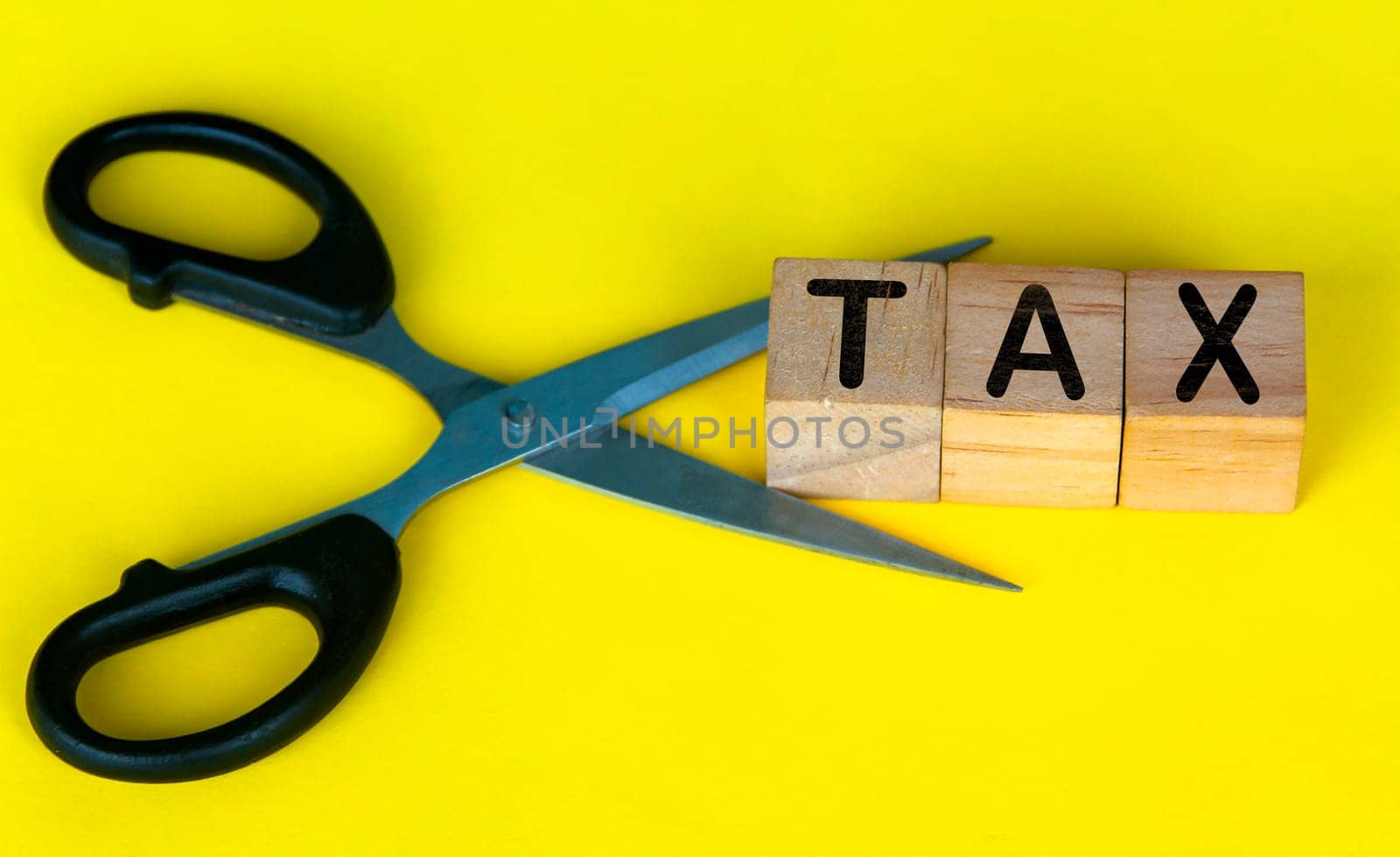 Scissor cutting wooden blocks with text TAX. Cutting tax expenses concept
