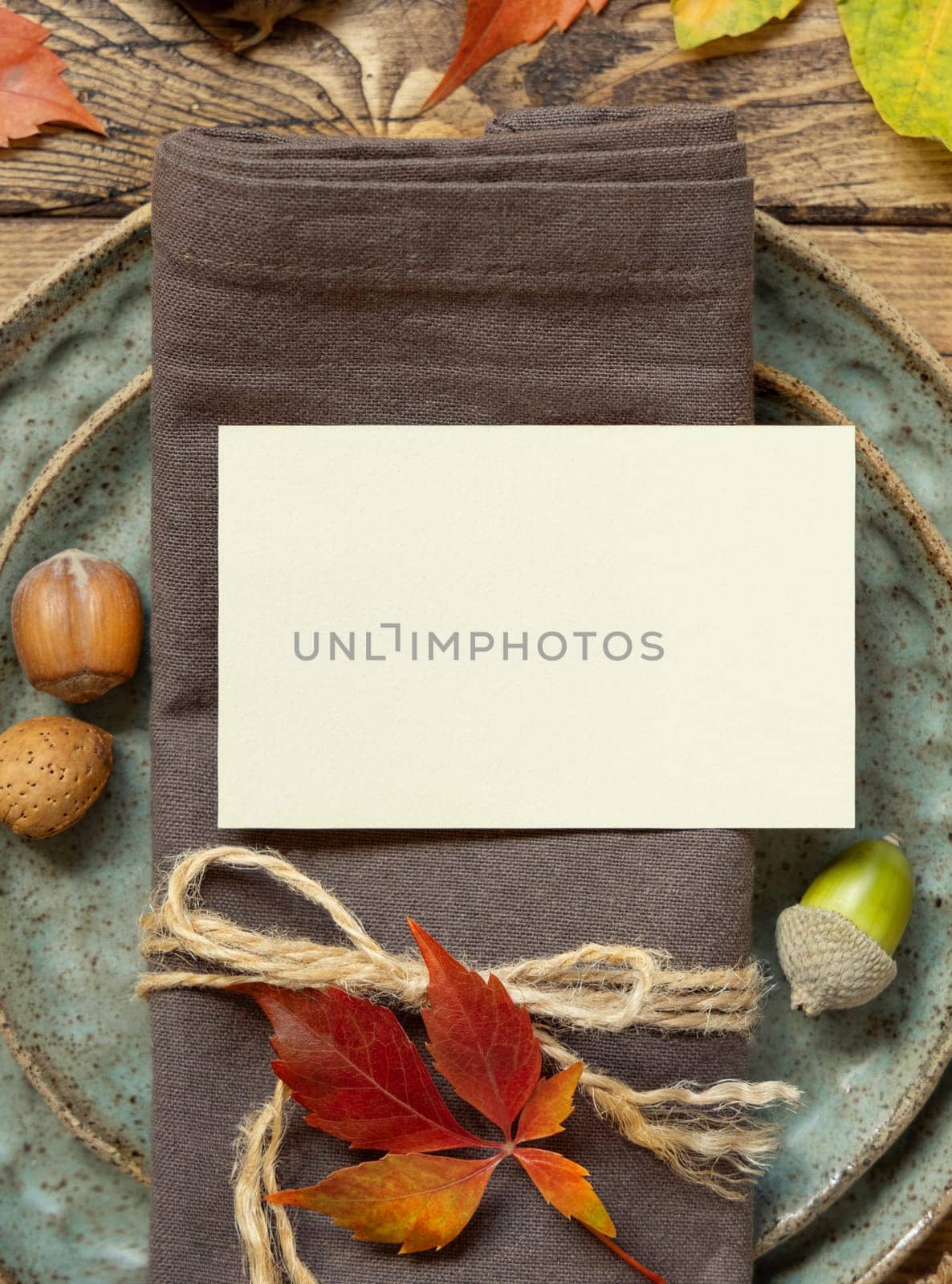 Autumn rustic table place with blank card between colorful leaves and berries, top view, mockup. Flat lay with horizontal card on wooden table, copy space. Thanksgiving or harvest concept