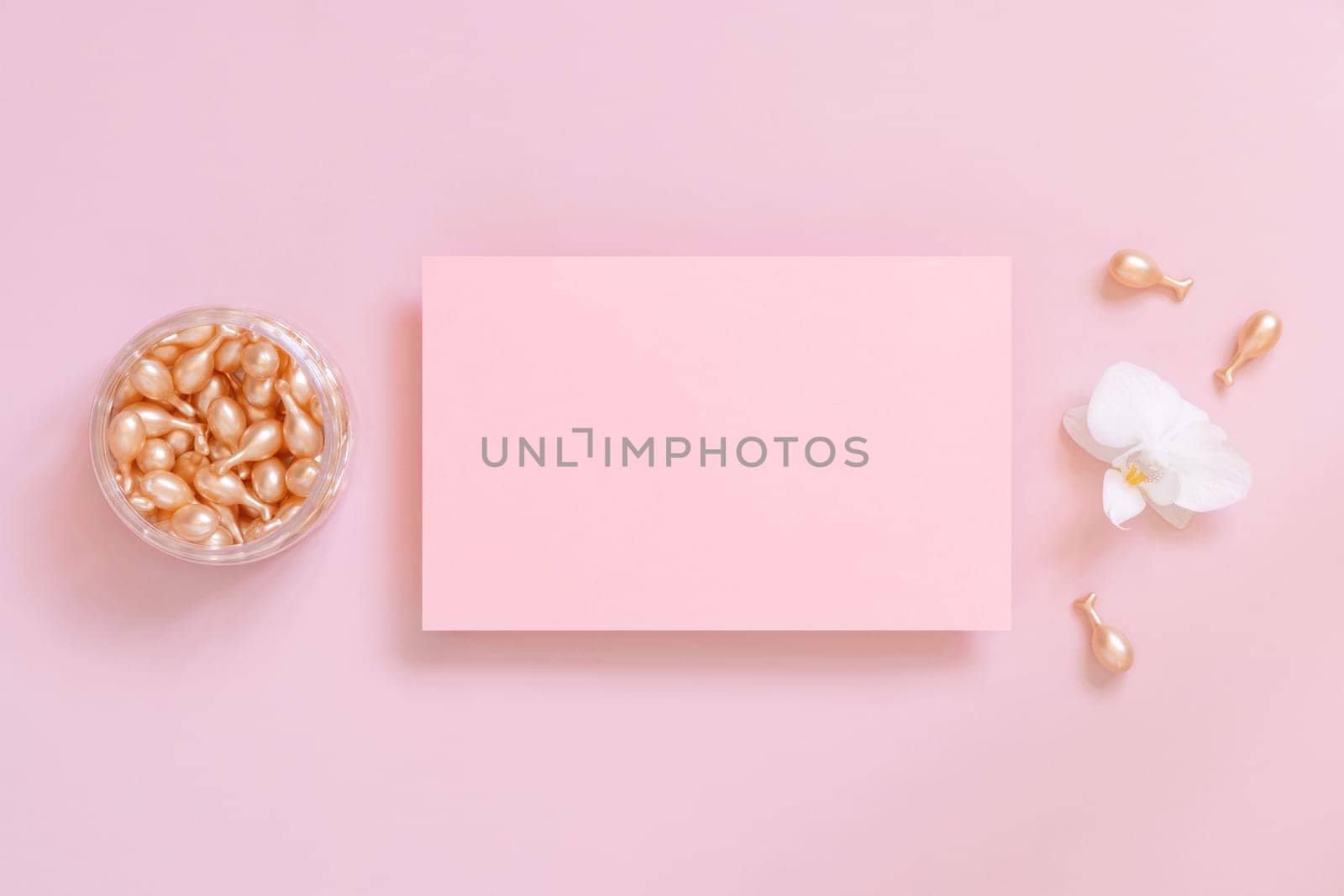 Blank card near Face serum capsules and white orchid flower on pink top view. Mockup. Facial treatment. Exotic minimal flat lay with copy space..