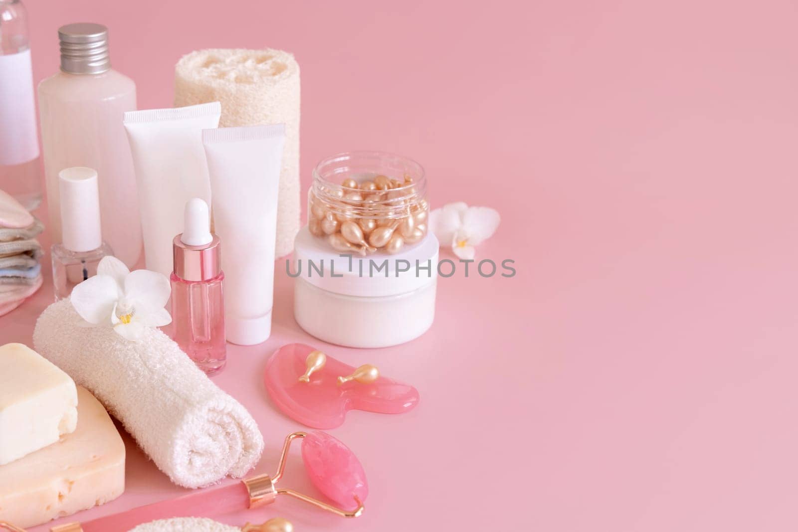 Natural cosmetic jars, skin care accesories and rose quartz face massagers with white orchid flower on light pink close up. Beauty products mockup. Everyday woman face care routine, Spa Treatments