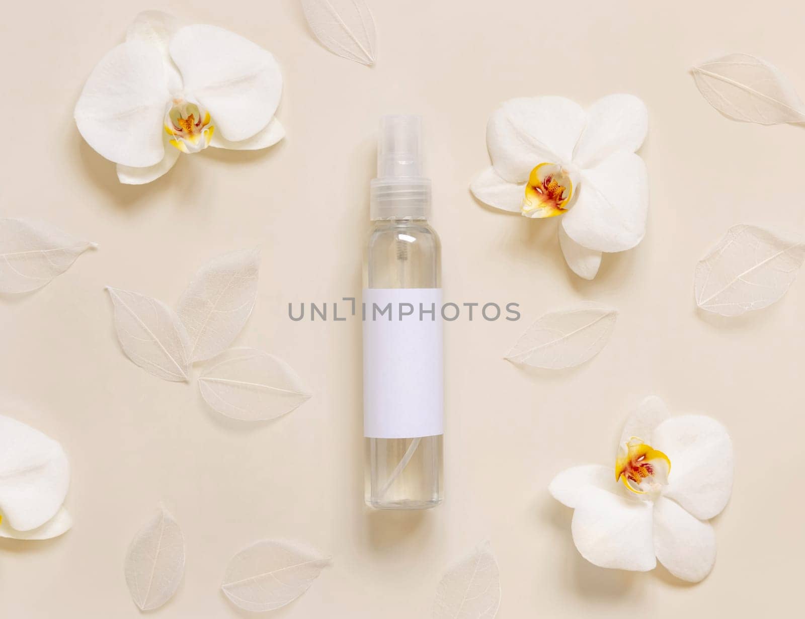 One pump dispenser bottle near white orchid flowers on light yellow top view, mockup. Skincare beauty product package. Exotic natural cosmetics, pastel minimal composition..