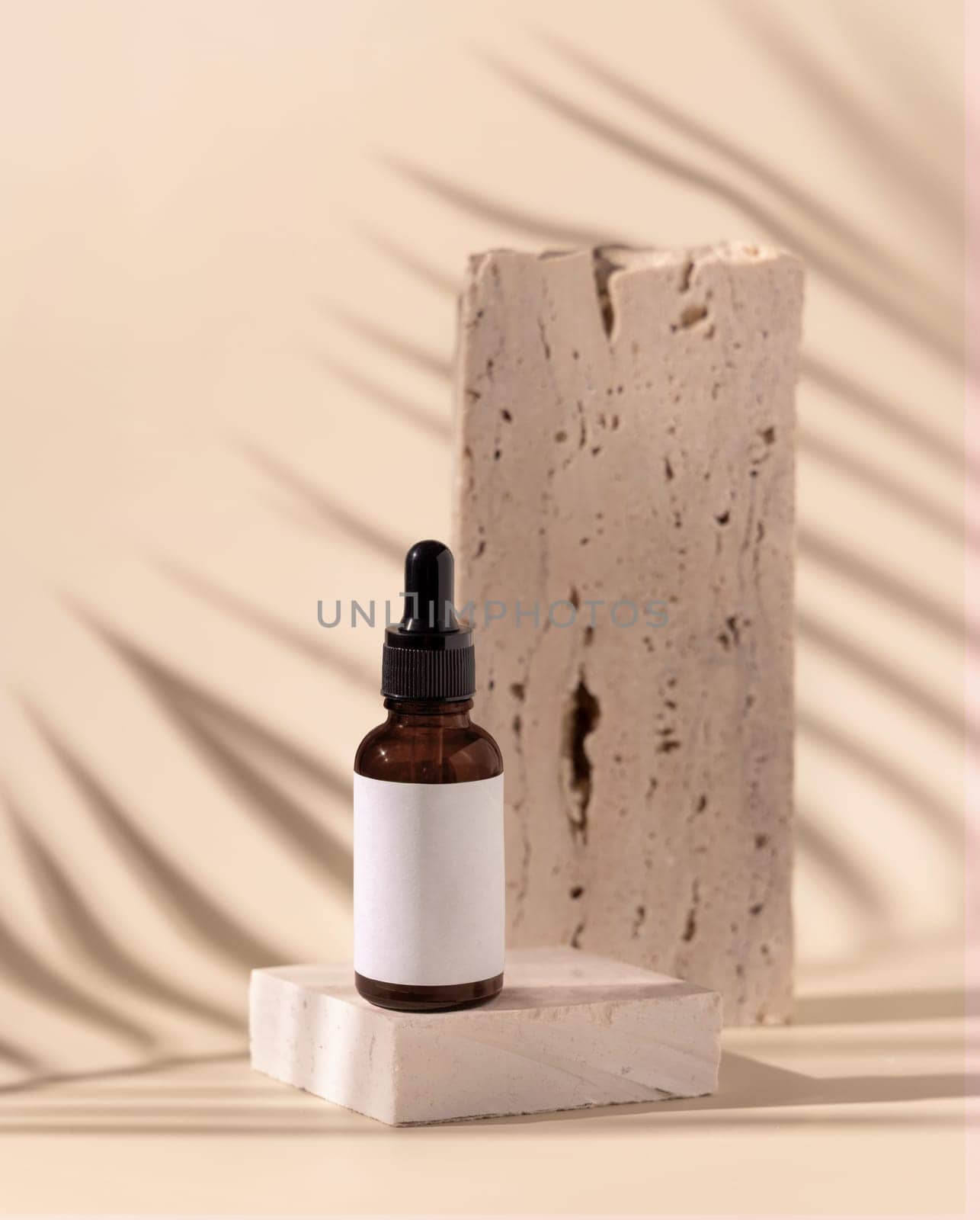 Glass cosmetic Dropper Bottle on travertine stone and palm leaf shadow on light yellow, close up, mockup. Skincare beauty product, essential oil or serum. Exotic cosmetics, pastel minimal composition..
