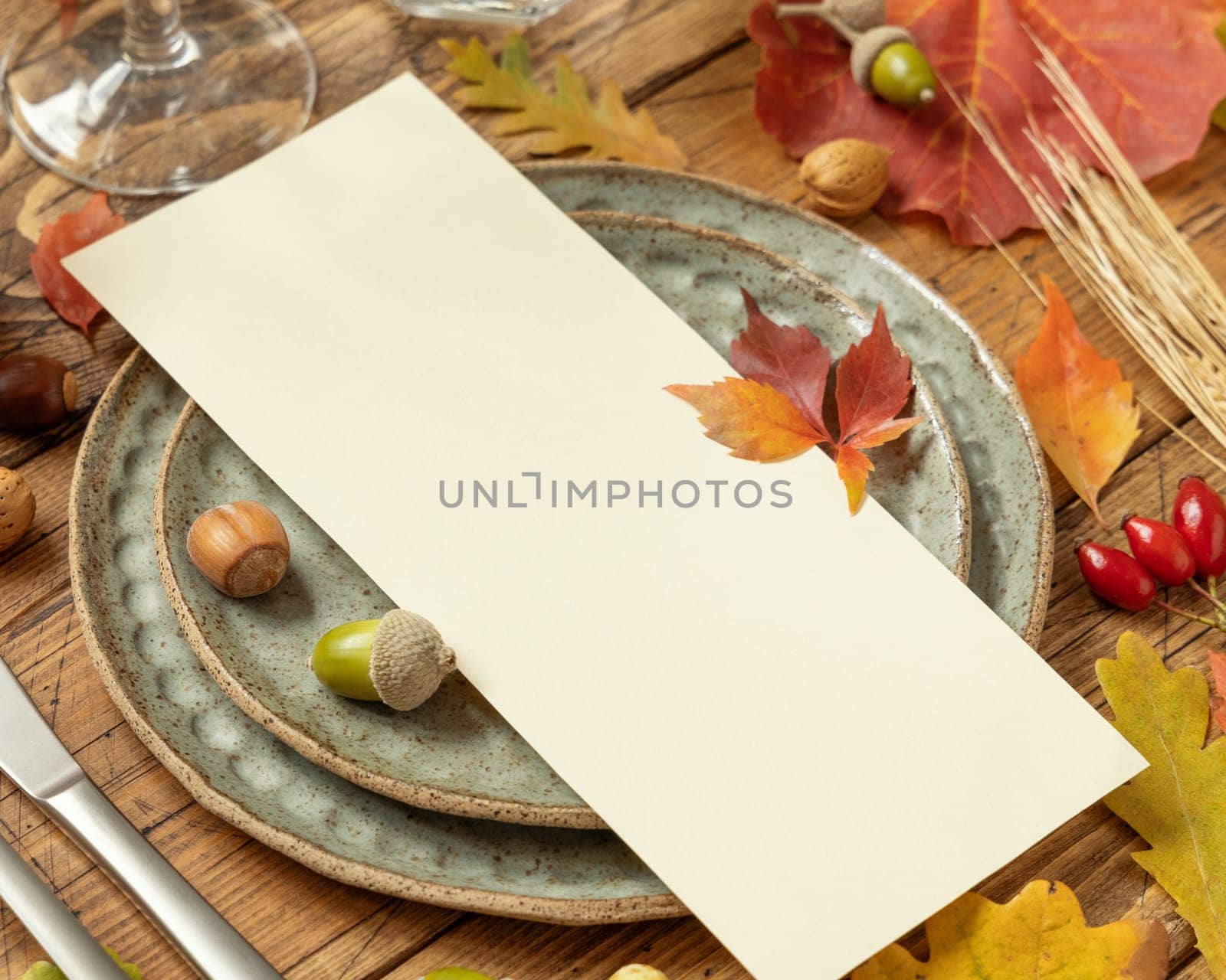 Autumn table setting with red, yellow and orange leaves, berries and blank card close up. Fall Mockup of vertical menu card on wooden table, copy space. Harvest, Halloween and Thanksgiving season