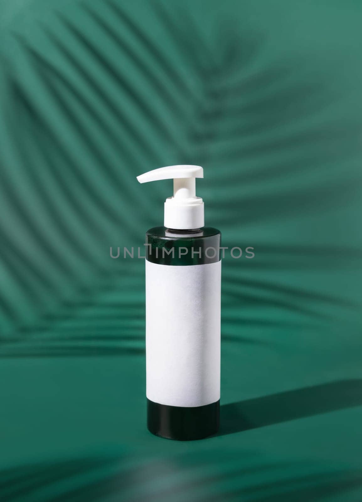 One pump Plastic bottle with blank label on green, palm leaf hard shadows, close up, mockup. Skincare beauty product, facial cleaner or lotion. Natural cosmetics..