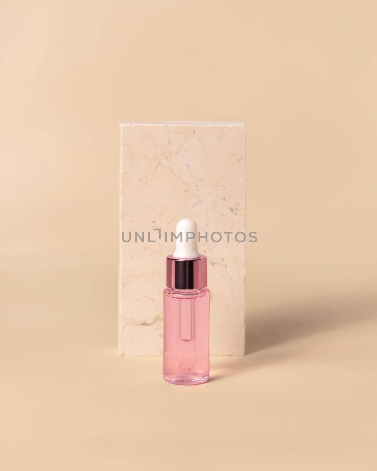 Glass cosmetic Dropper Bottle near travertine stone on light yellow, close up, mockup. Exotic skincare beauty product, essential oil or serum. Pastel minimal composition..