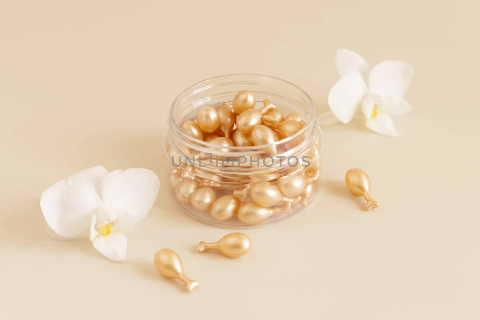 Beauty serum capsules in a jar near white orchid flowers on light yellow close up. Skincare cosmetics. Facial treatment with perfect dosage of serum to be used. Pastel composition..