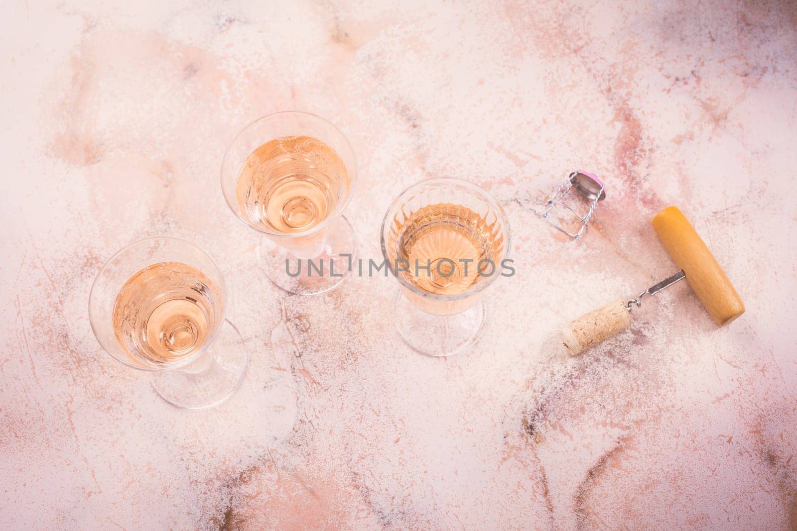 Three glasses of rose wine at wine tasting with bottle opener on pink marble background