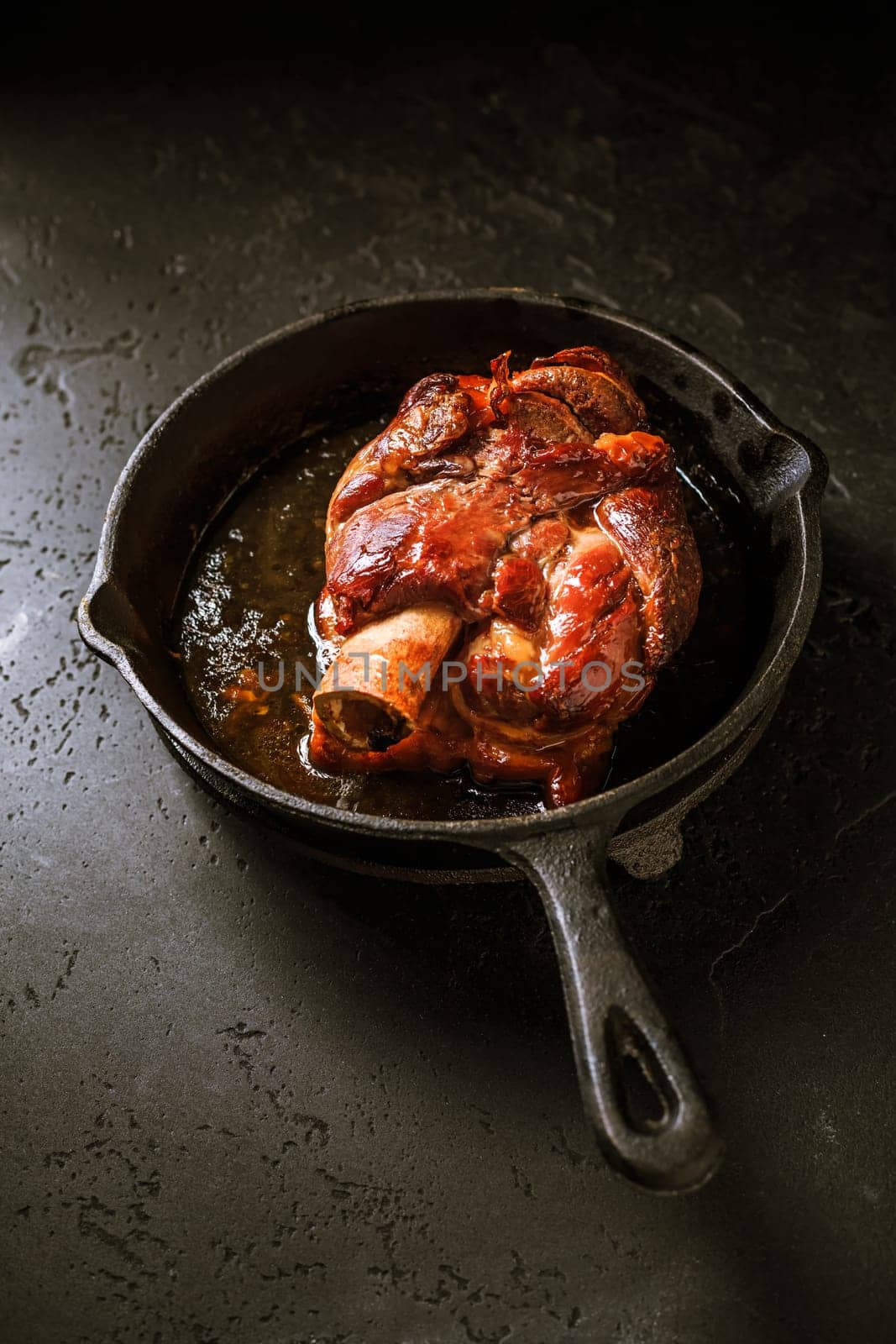 Traditional German cuisine - Roasted pork knuckle eisbein (Schweinshaxe) in iron pan on black background