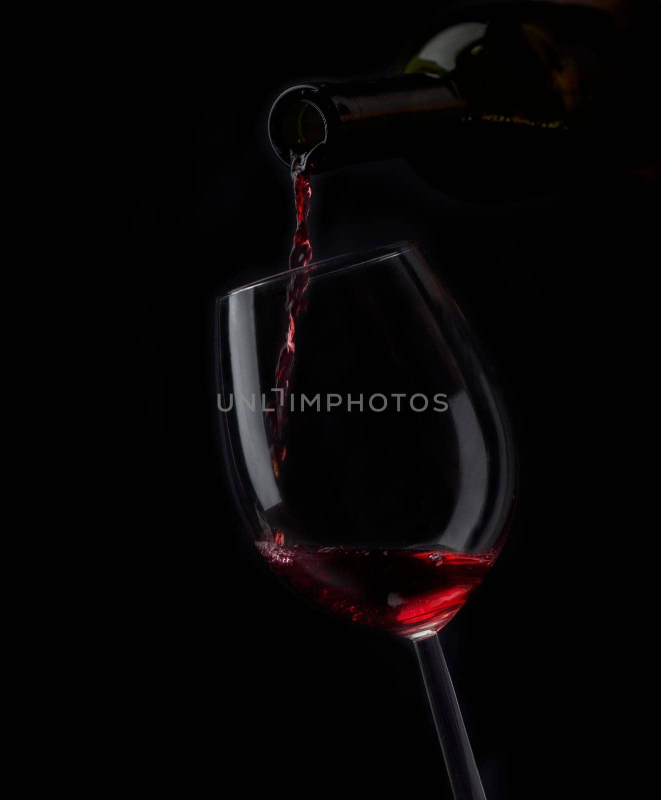 Red wine pouring in wineglass from bottle over black background. Wine list design menu with copyspace. Alcohol beverage card backdrop.