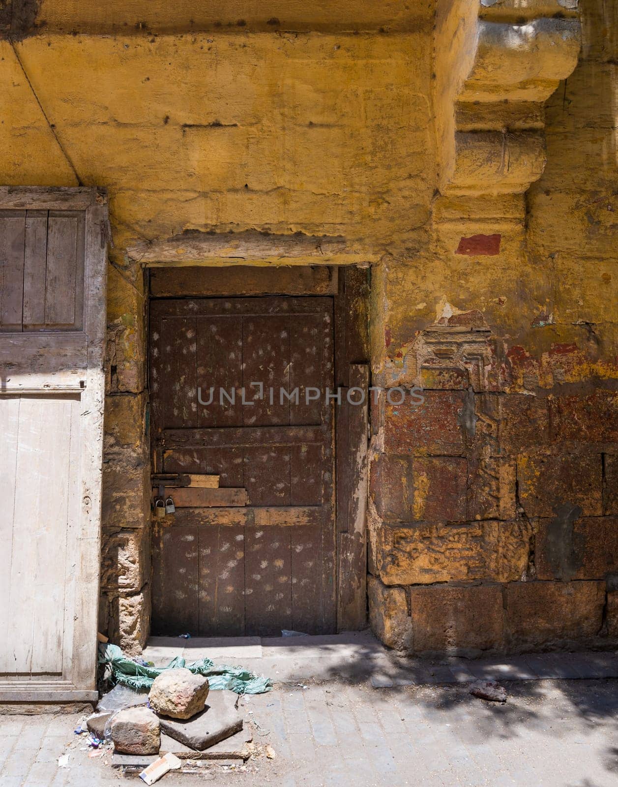 Broken wooden brown door on grunge stone bricks wall painted in orange in abandoned Darb El Labana district, Cairo, Egypt