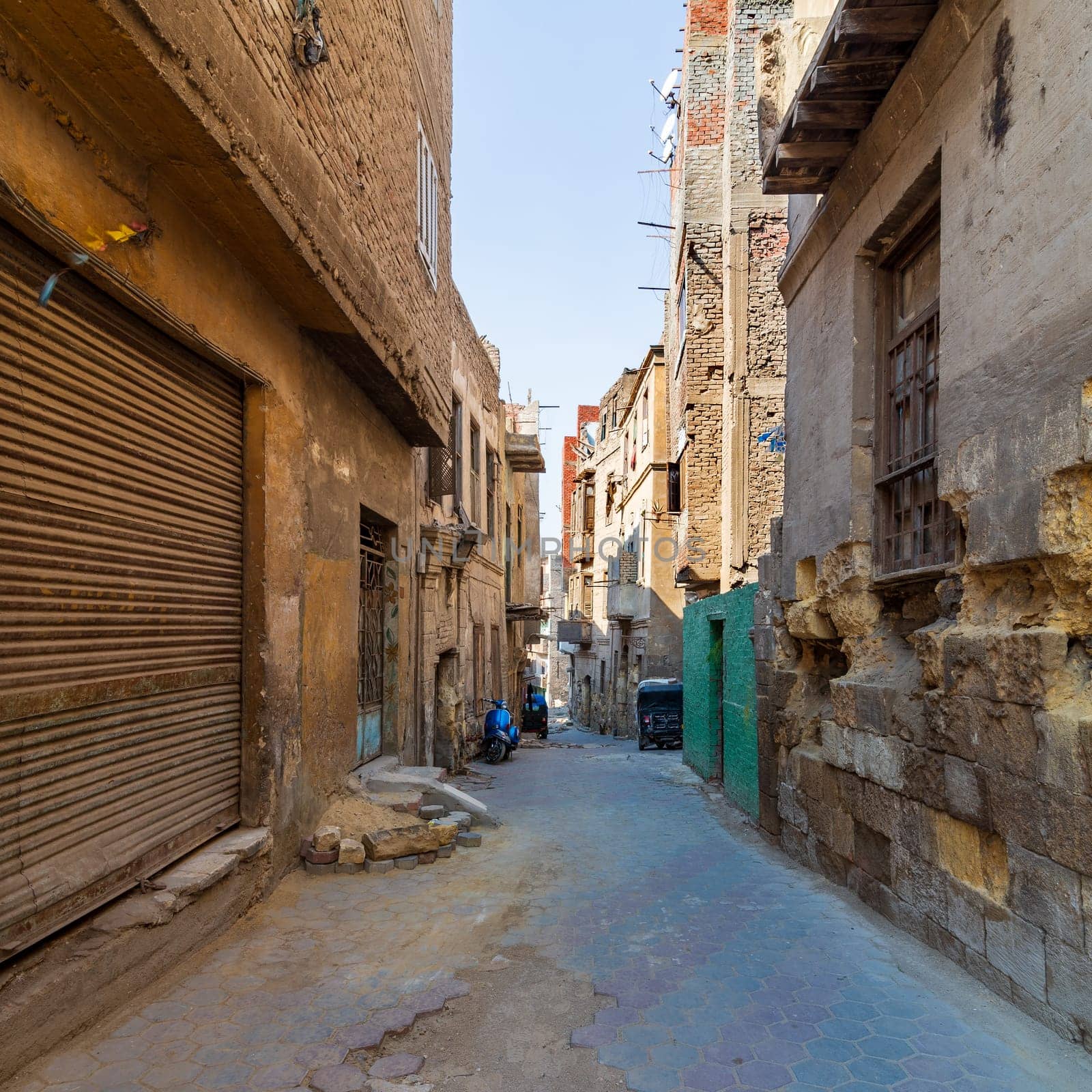 Aged houses with crumbling walls located on narrow abandoned street on sunny day in old Cairo, Egypt