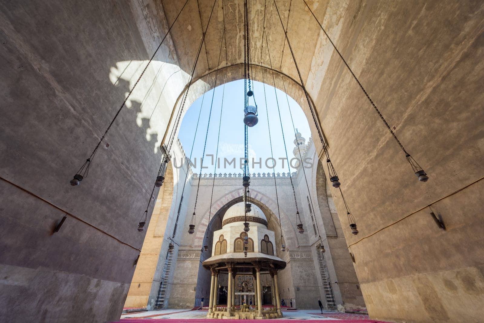 Cairo, Egypt - December 16, 2017: Courtyard of the Mosque of Sultan Hasan with Ablution fountain and huge arch, and few tourists visiting the place at the early morning