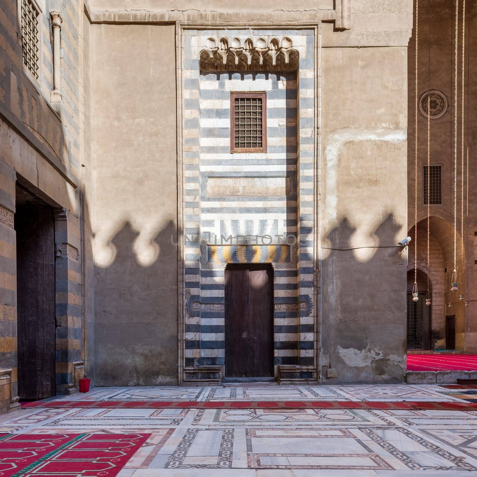 Wall with striped black and white marble decorations, wooden grunge door and window at the courtyard of historic public mosque of Sultan Hassan, Cairo, Egypt