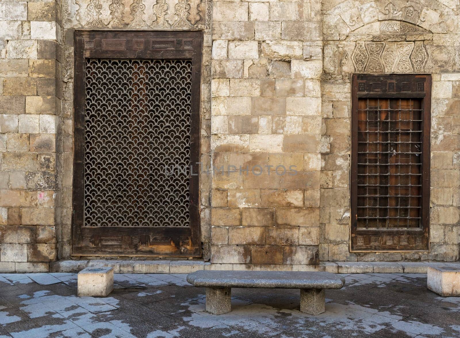 Two wooden windows with decorated iron grid over stone bricks wall and marble garden bench, Moez Street, Cairo, Egypt
