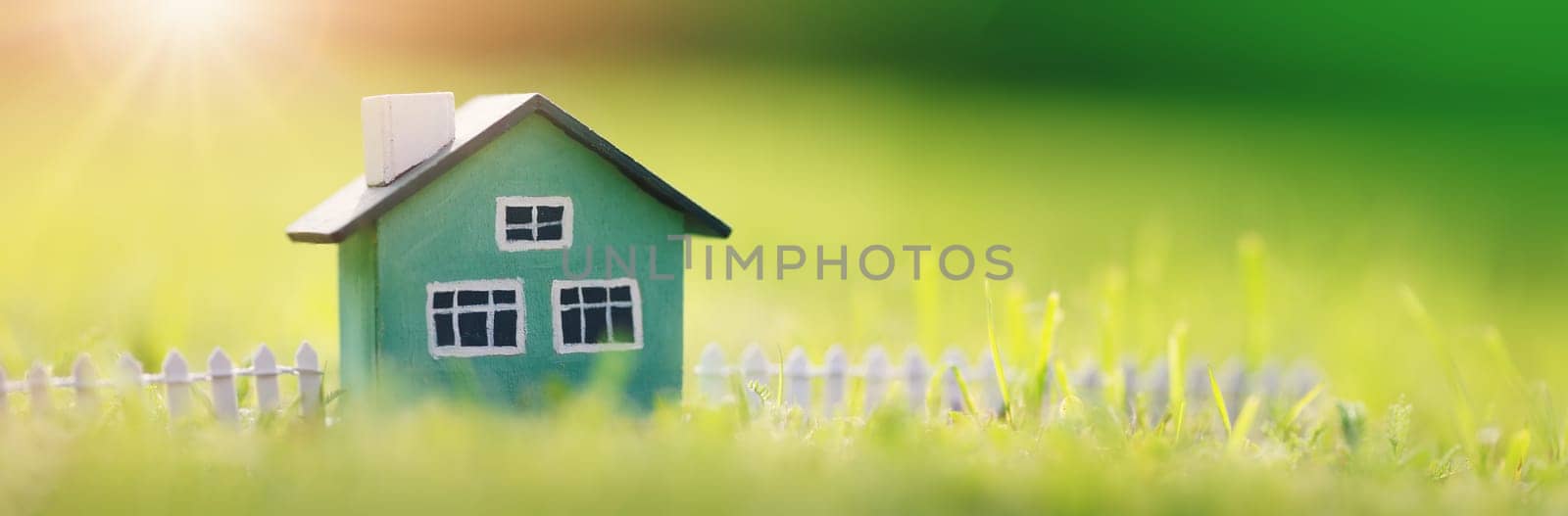 Green house model with fence standing on the green grass. Panoramic view. Conceptual symbol of the buying a new house or ownership of real estate.