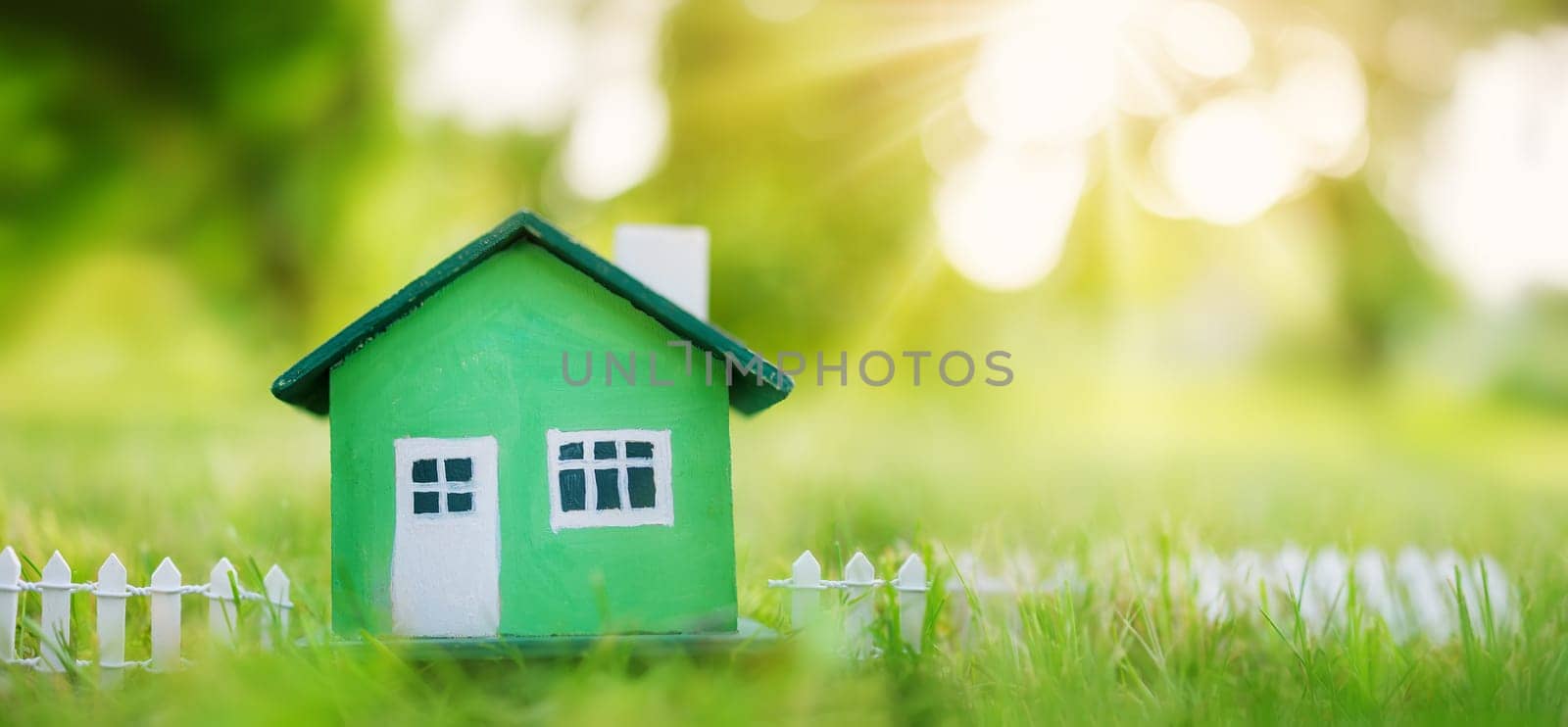 Green house model with fence standing on the green grass. Panoramic view. Conceptual symbol of the buying a new house or ownership of real estate.