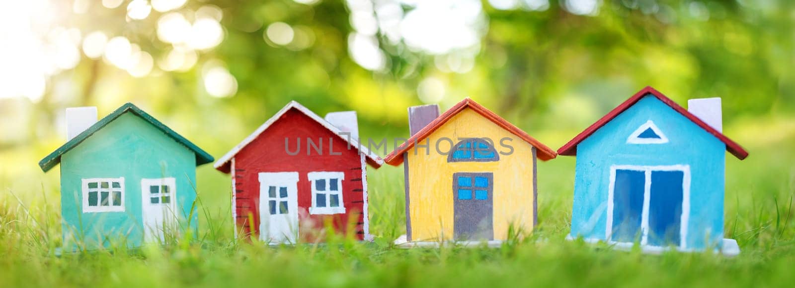 Several colourful houses models standing on the green grass. Panoramic view. Conceptual symbol of the buying a new house or ownership of real estate.