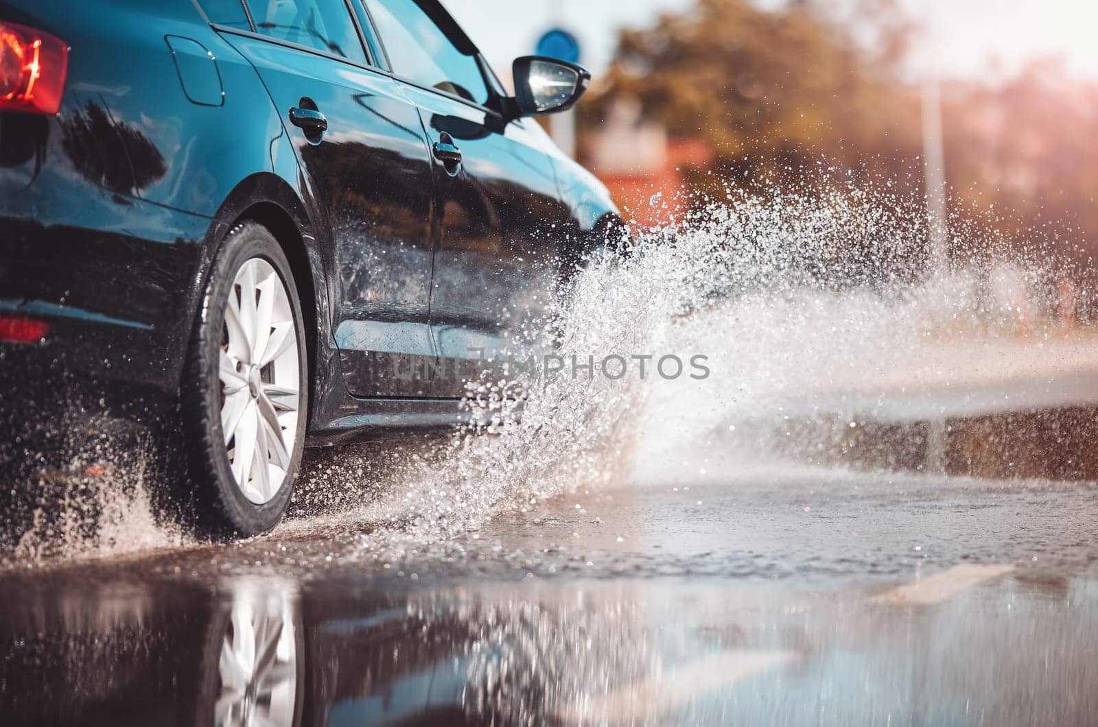Car driving through the puddle and splashing by water. Dangerous situation. Concept of road safety.