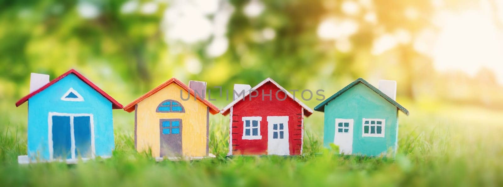 Several colourful houses models standing on the green grass. Panoramic view. Conceptual symbol of the buying a new house or ownership of real estate.
