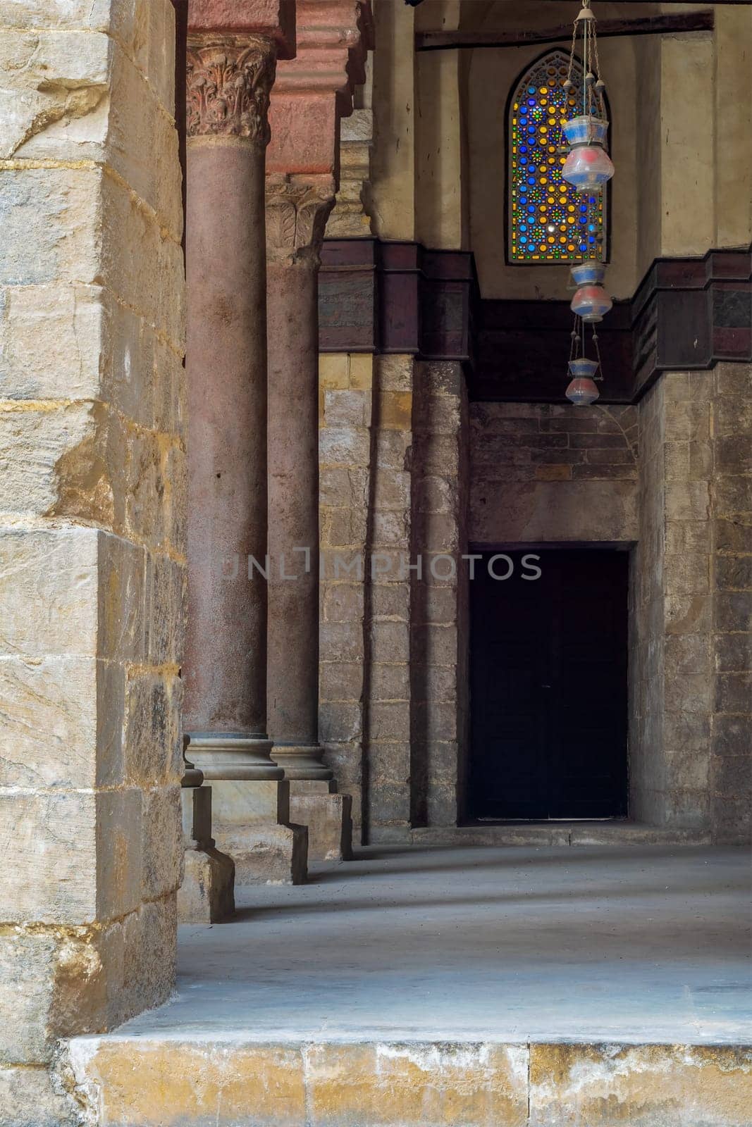 Passage at Sultan Qalawun Mosque with stone columns, colored stained glass windows and wooden door, Cairo, Egypt