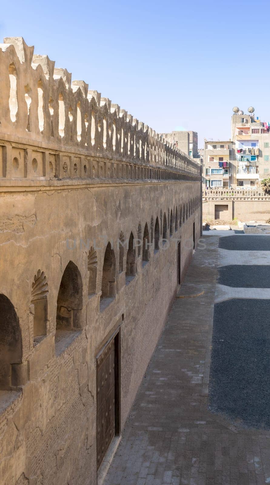 Stone bricks old weathered fence with wooden doors, arched stucco window, and floral engraved decorations, Ibn Tulun mosque, Sayyida Zaynab district, Medieval Cairo, Egypt