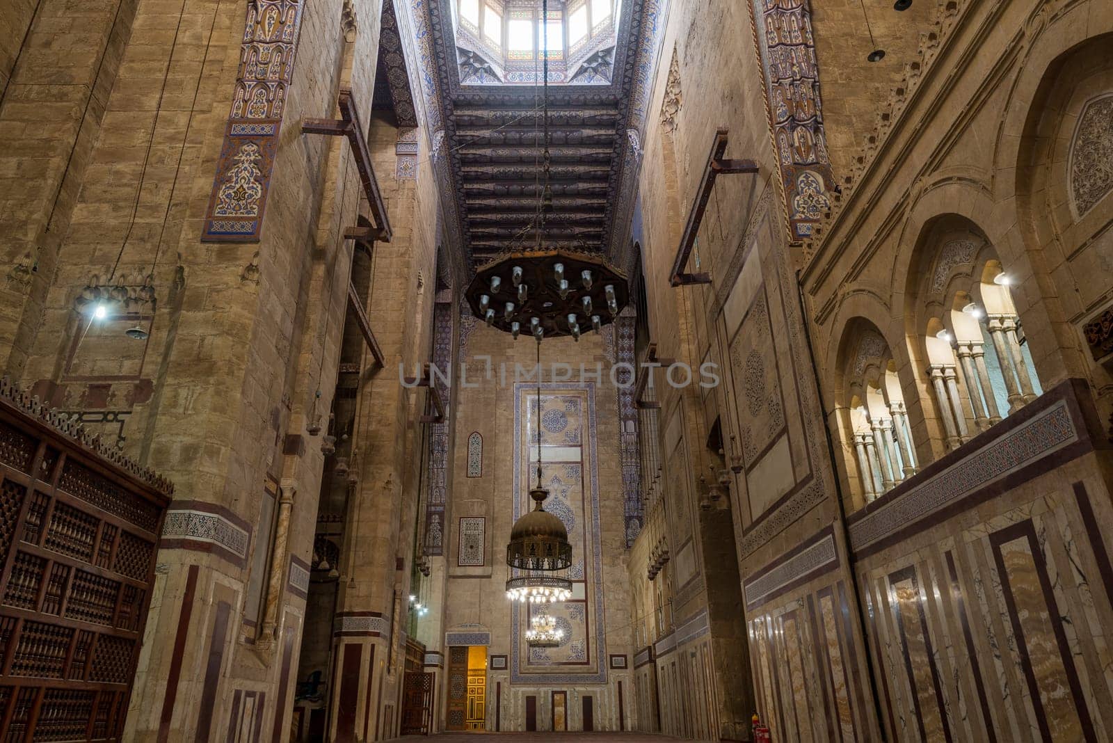 Interior of al Refai mosque with old decorated bricks stone wall, colored marble decorations, wooden ornate ceiling, big brass chandeliers, and wooden latticework door, Cairo, Egypt