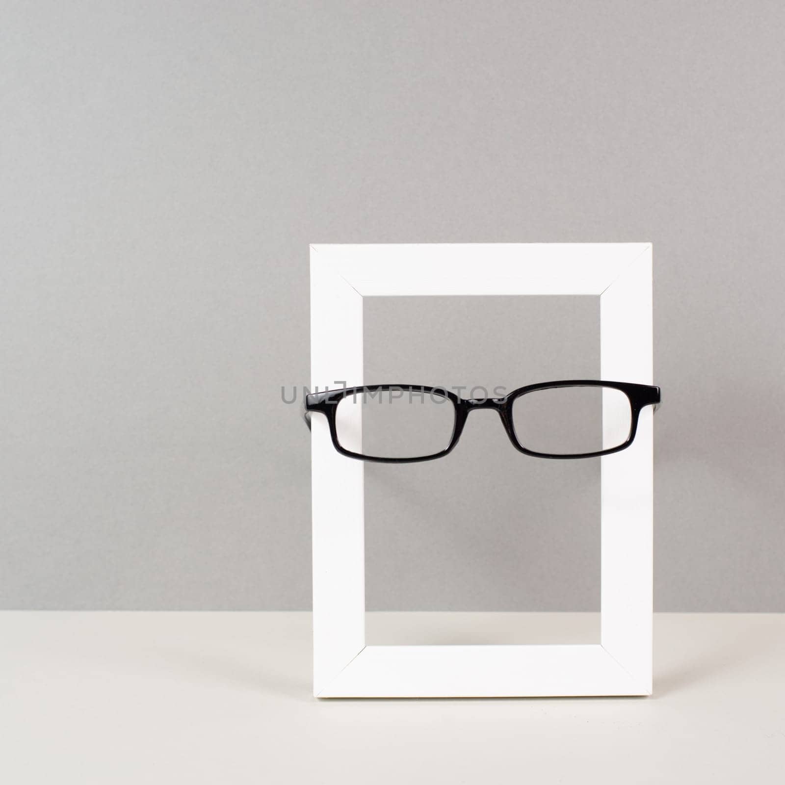 Home interior poster mock up with wooden frame and eyeglasses, gray wall background, copy space for text and pictures