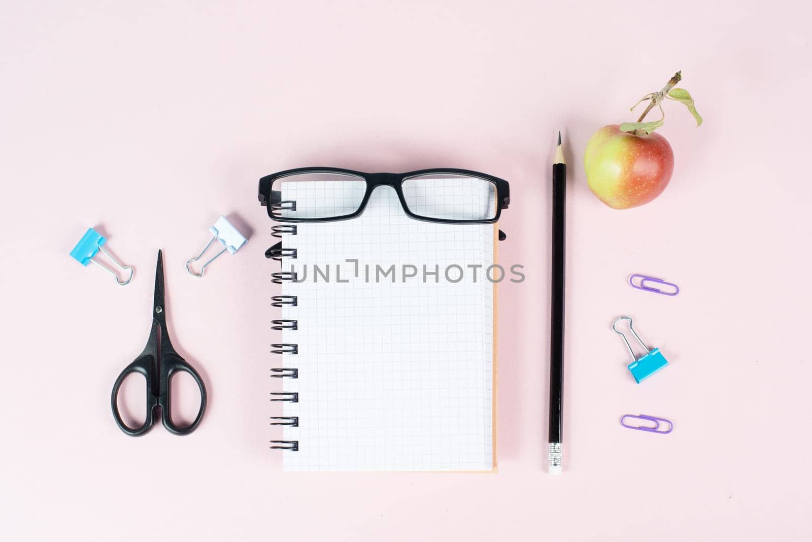 Empty notebook with a pen, eyeglasses and an apple on a pastel colored desk, brainstorming for new ideas, writing a message, home office and education concept
