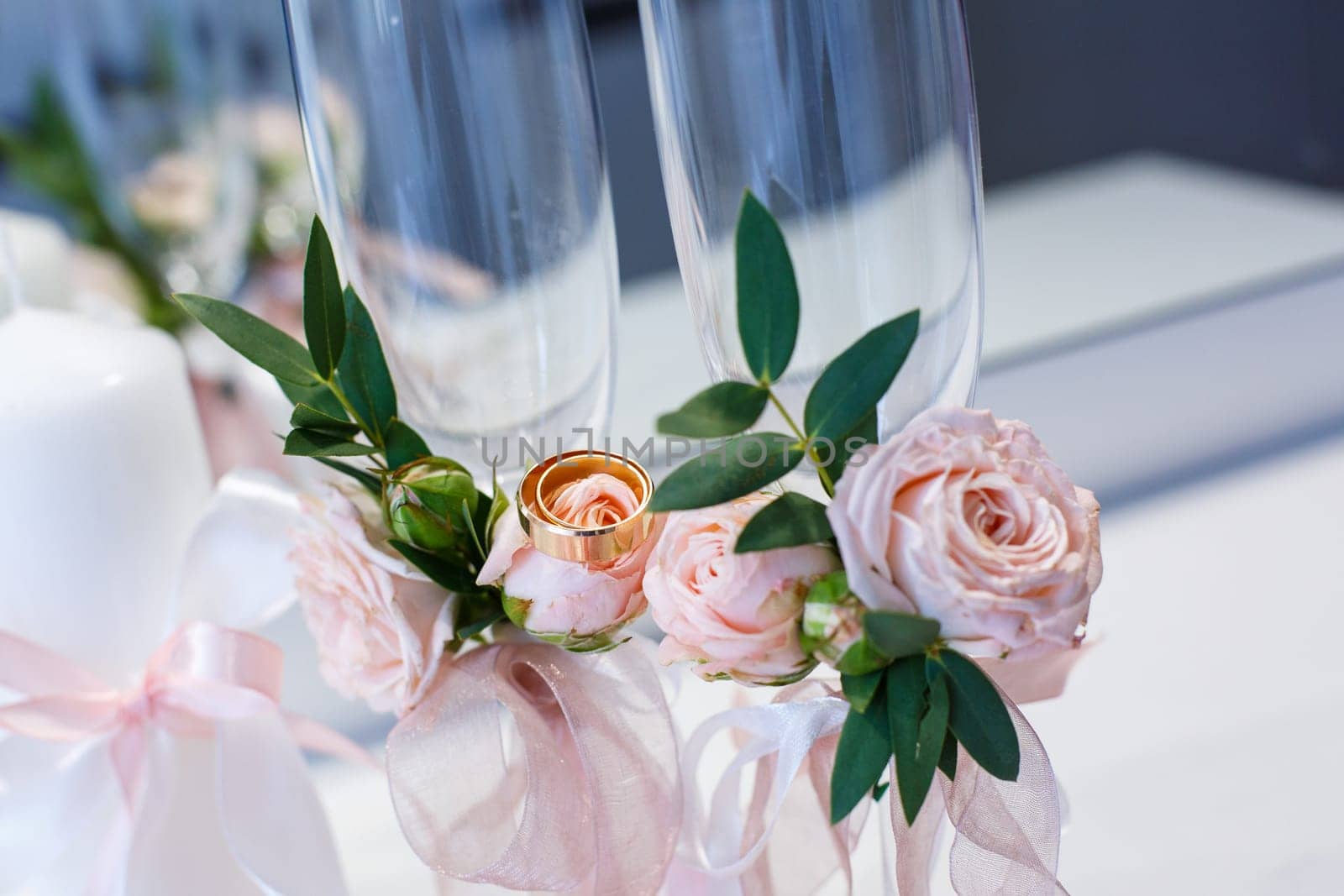 Two gold wedding rings close up lie on flowers decorating champagne glasses. Wedding details, symbol of love and marriage. Beautiful wedding background.