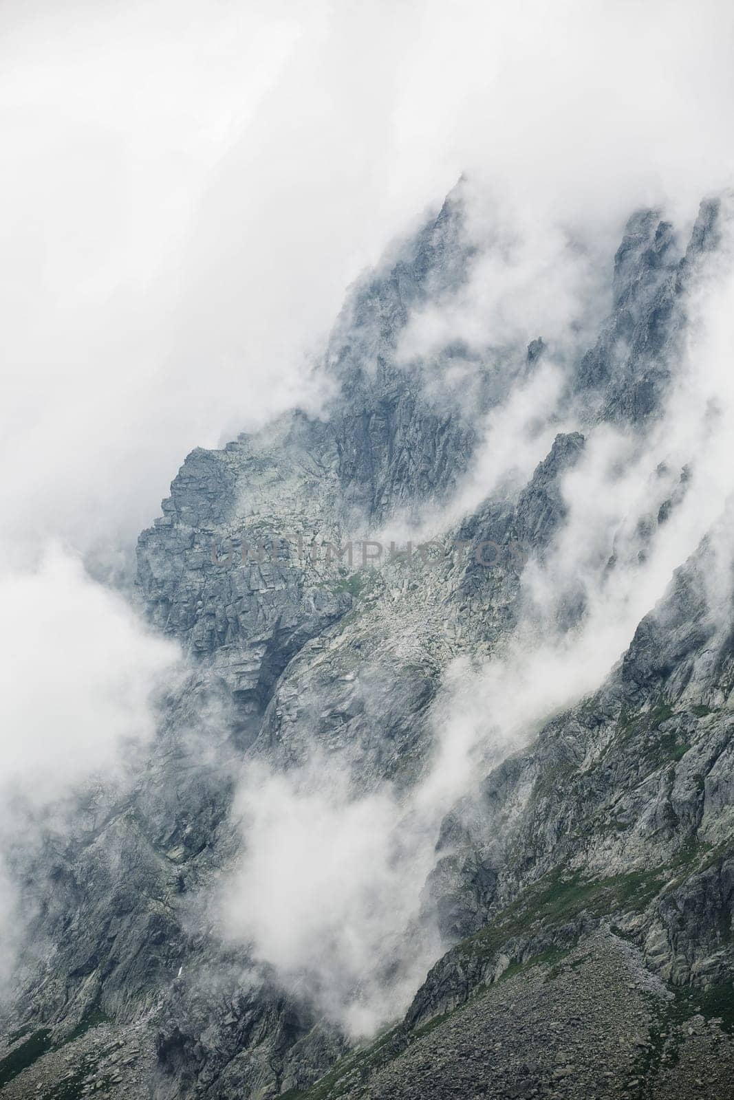 A mystical photo of rough rocky mountains surrounded by a white blanket of clouds