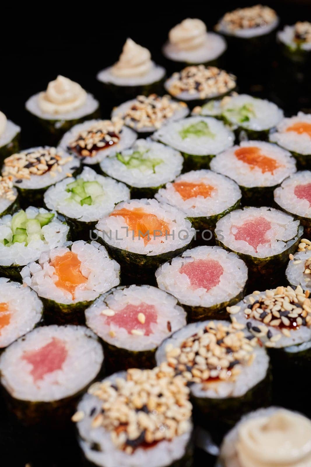 Large set of Maki rolls with a variety of fresh fish and vegetable fillings. Rolls with cream cheese, salmon, cucumber, sesame seeds and sauce. Selective focus.