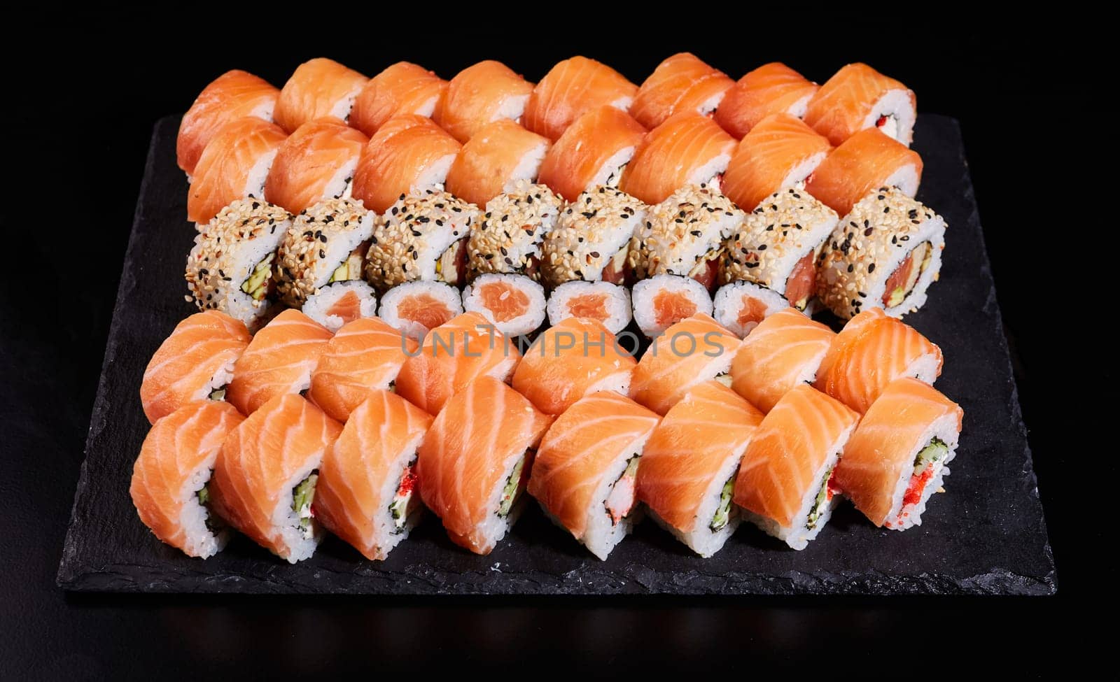 Sushi set which consists of a large number of roles of Philadelphia with raw salmon and other sushi in between. Japanese sushi set. Different types of rolls on a stone plate on a black background.