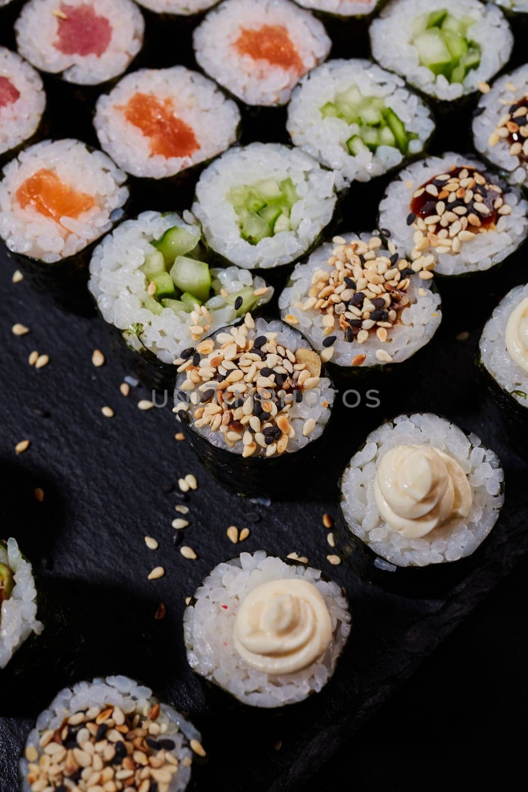 Top view Maki rolls with salmon, tuna, cucumber sesame and cream cheese lie on a black stone sushi board. Japanese traditional cuisine.