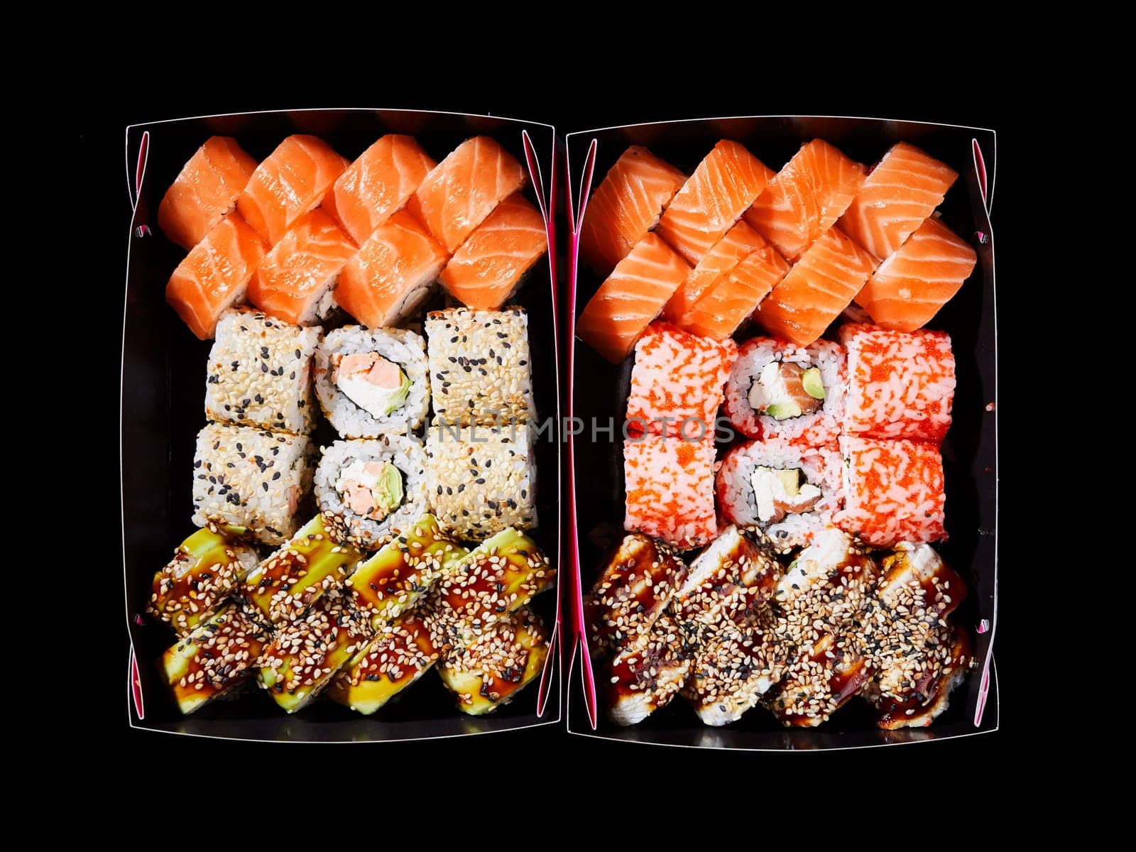 Top view of assorted sushi on a black background in two cardboard boxes ready for delivery. Rainbow sushi rolls, uramaki, hosomaki and nigiri. Concept of delivery of delicious original sushi sets.