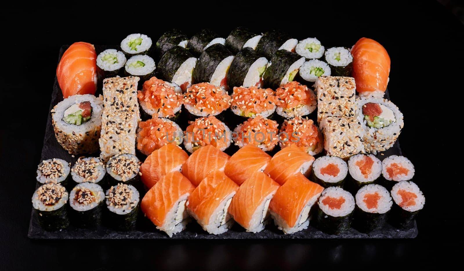 Assortment of different types of sushi rolls placed on a black stone board. Menu sushi with nigiri, maki, uramaki for ordering in a restaurant or delivery. Japanese Oriental Cuisine.