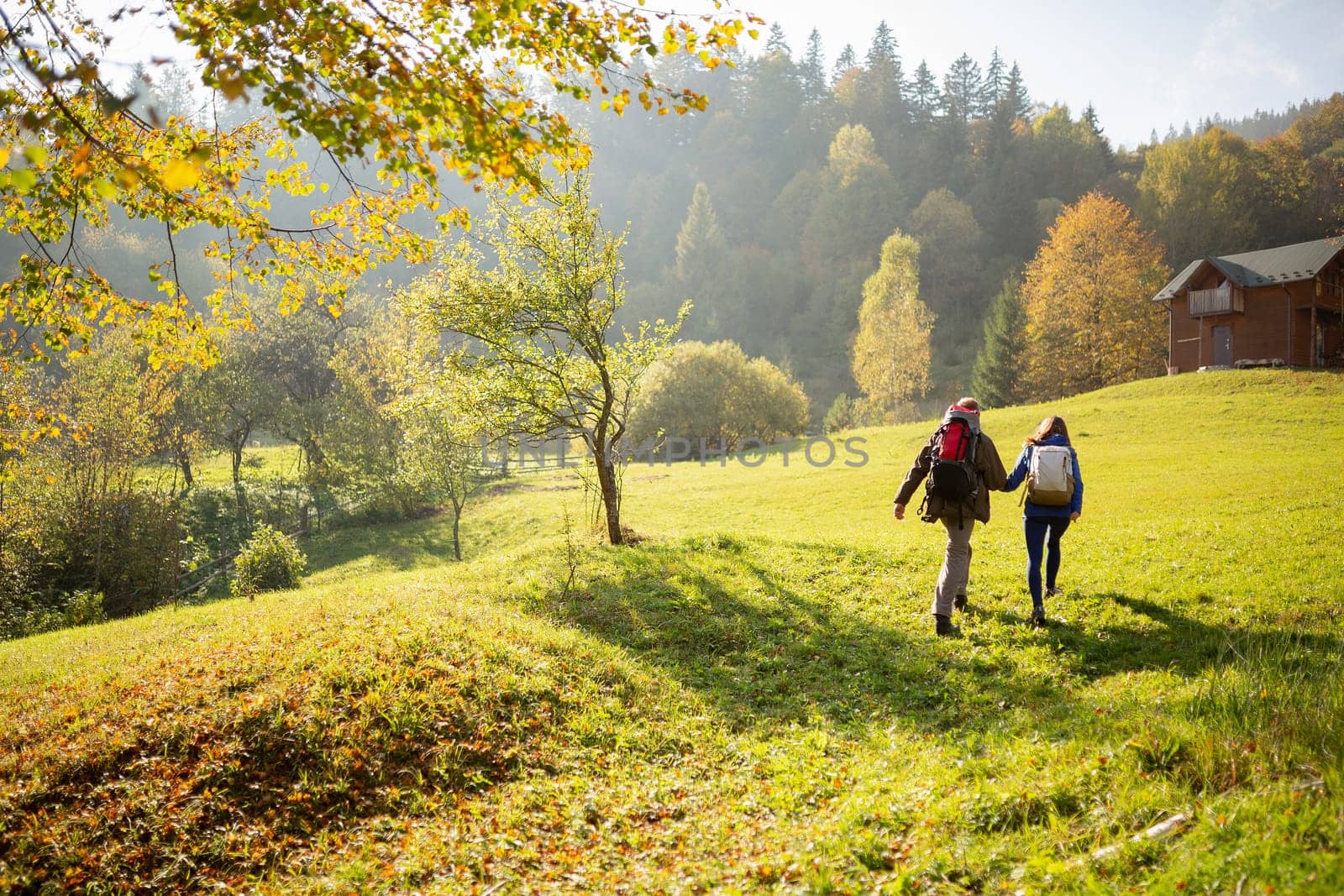 Active tourism. Rear view of a young couple of travelers who lead an adventurous lifestyle and travel in the mountains go to a wooden house to relax. Concepts about travel, lifestyle and wanderlust.