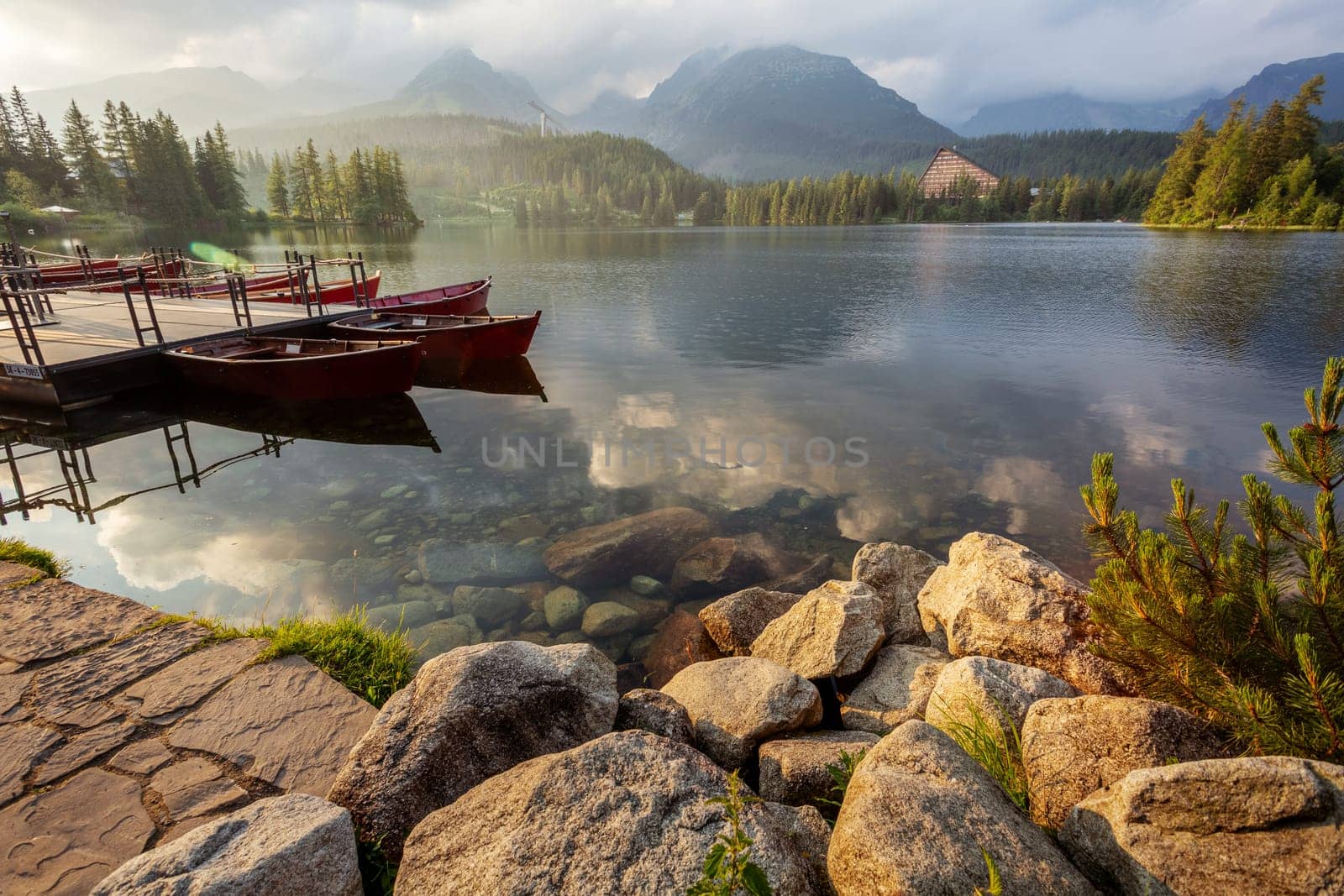 View of a mountain lake Strbske pleso in the High Tatras. Slovakia. Boats on the water glow in the sun at sunrise.