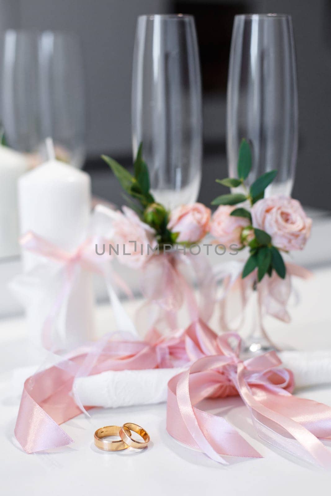 Wedding accessories. Rings and wedding details in pink style, which are on the table. Wedding rings lie on the table near the candles with pink ribbons and glasses decorated with pink flowers.