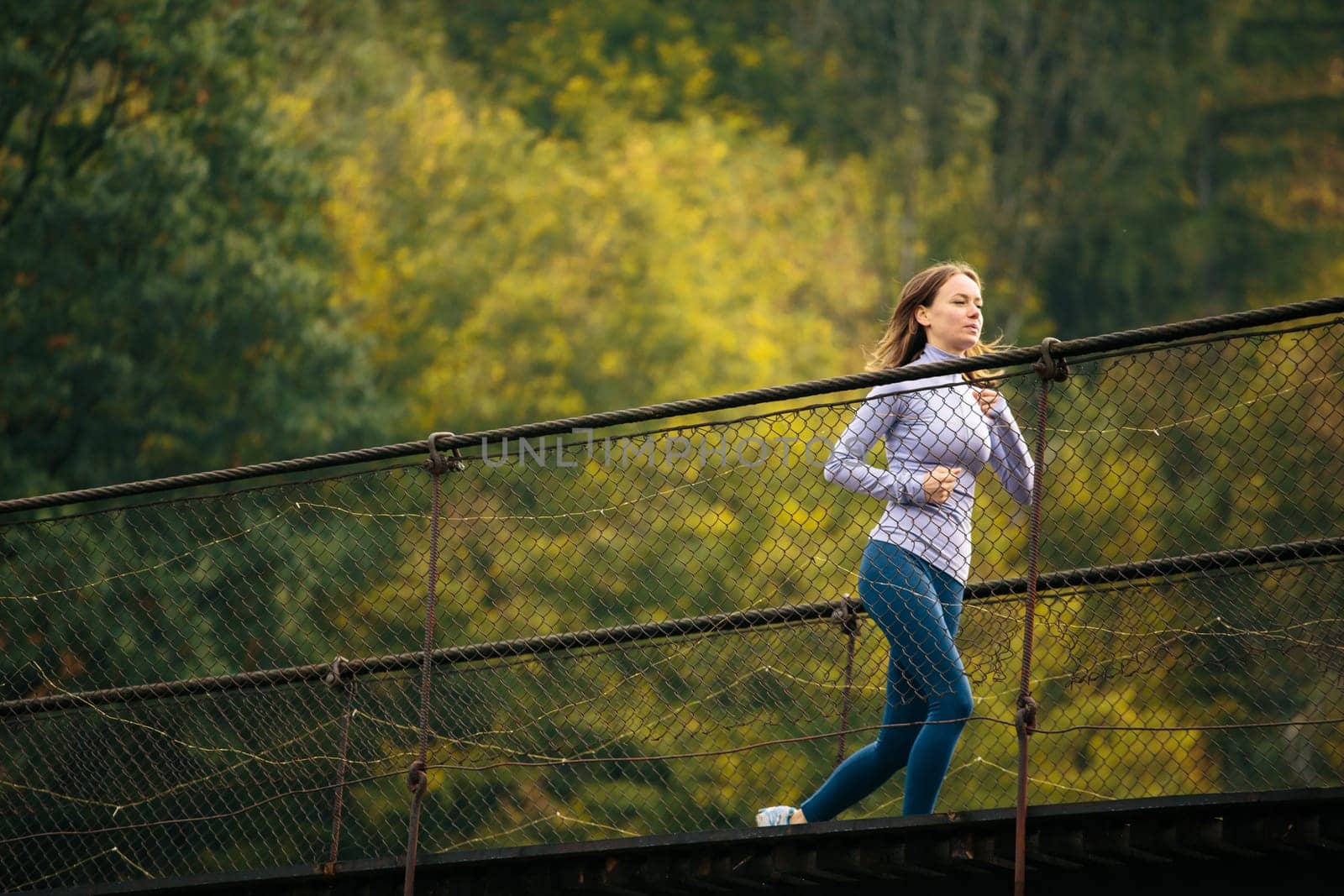 Morning sports run. Young female athlete in the morning jogging on a suspension bridge on a background of green mountain forest. Jogging, active lifestyle concept.