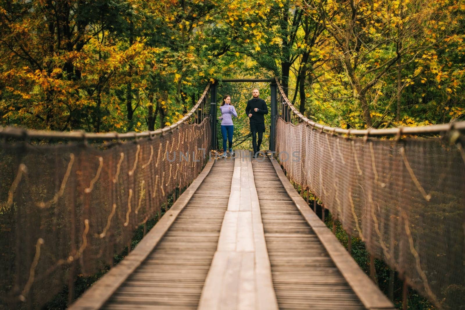 Fitness and sports motivation. Young runners man and woman start jogging on a wooden suspension bridge in the middle of a mountain forest. Concept of a healthy and active lifestyle.