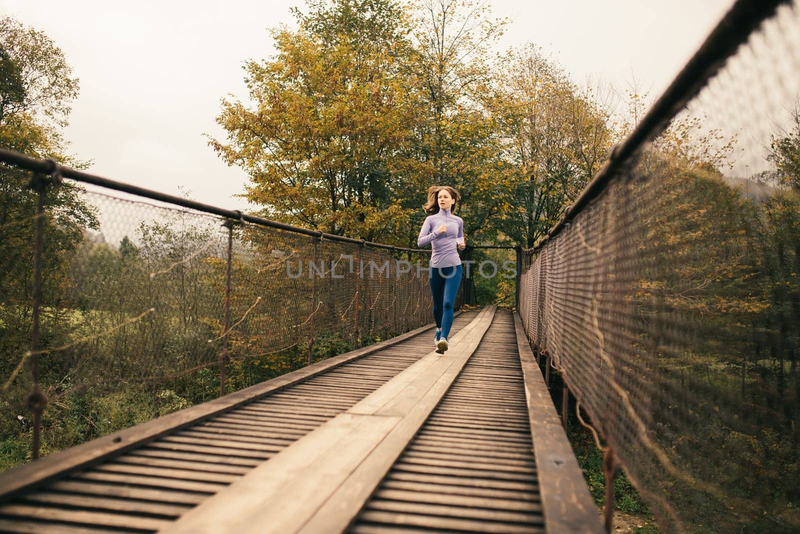 Early morning workout. Slender athletic young woman in the morning jogging on a suspension bridge in a mountain village. Healthy lifestyle. Fitness, sport, people, exercising and lifestyle concept