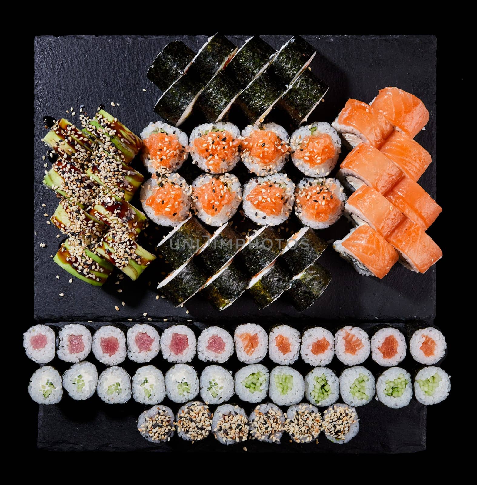 Sushi rolls of Japanese cuisine on a stone board. Different types of sushi roll set with different fish, vegetables, cheese, sesame and avocado on a gray textured board. Japanese restaurant menu.