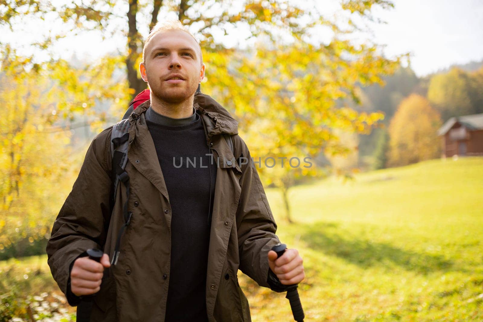 Close up portrait of a tourist man who travels in the mountains and rejoices when he sees his goal in the distance. Man with trekking sticks stands on a background of autumn mountain nature. Blurred.