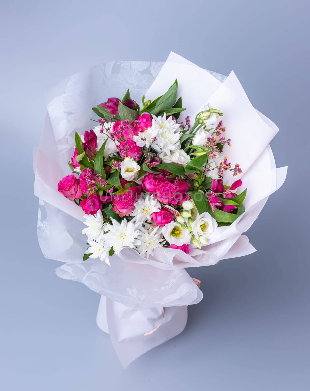 Big bouquet of pink and white flowers wrapped in bright floral paper on a blue background. Festively packed bouquet with pink peonies, white chrysanthemums and eustoma. Concept of floral arrangements.